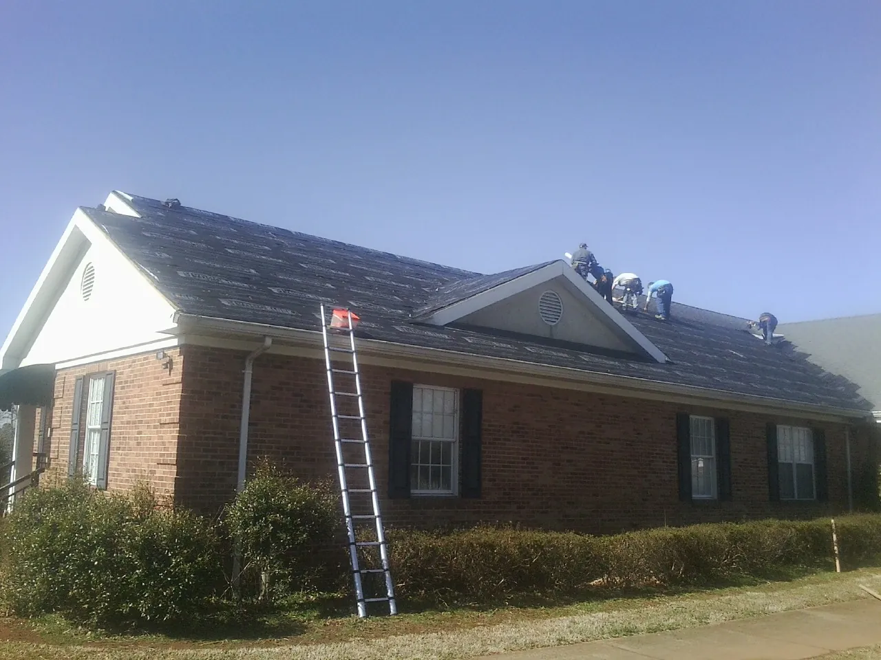 Crew tearing shingles off a brick ranch roof with a ladder set — Emergency Roof Repair work by our crew in Cope