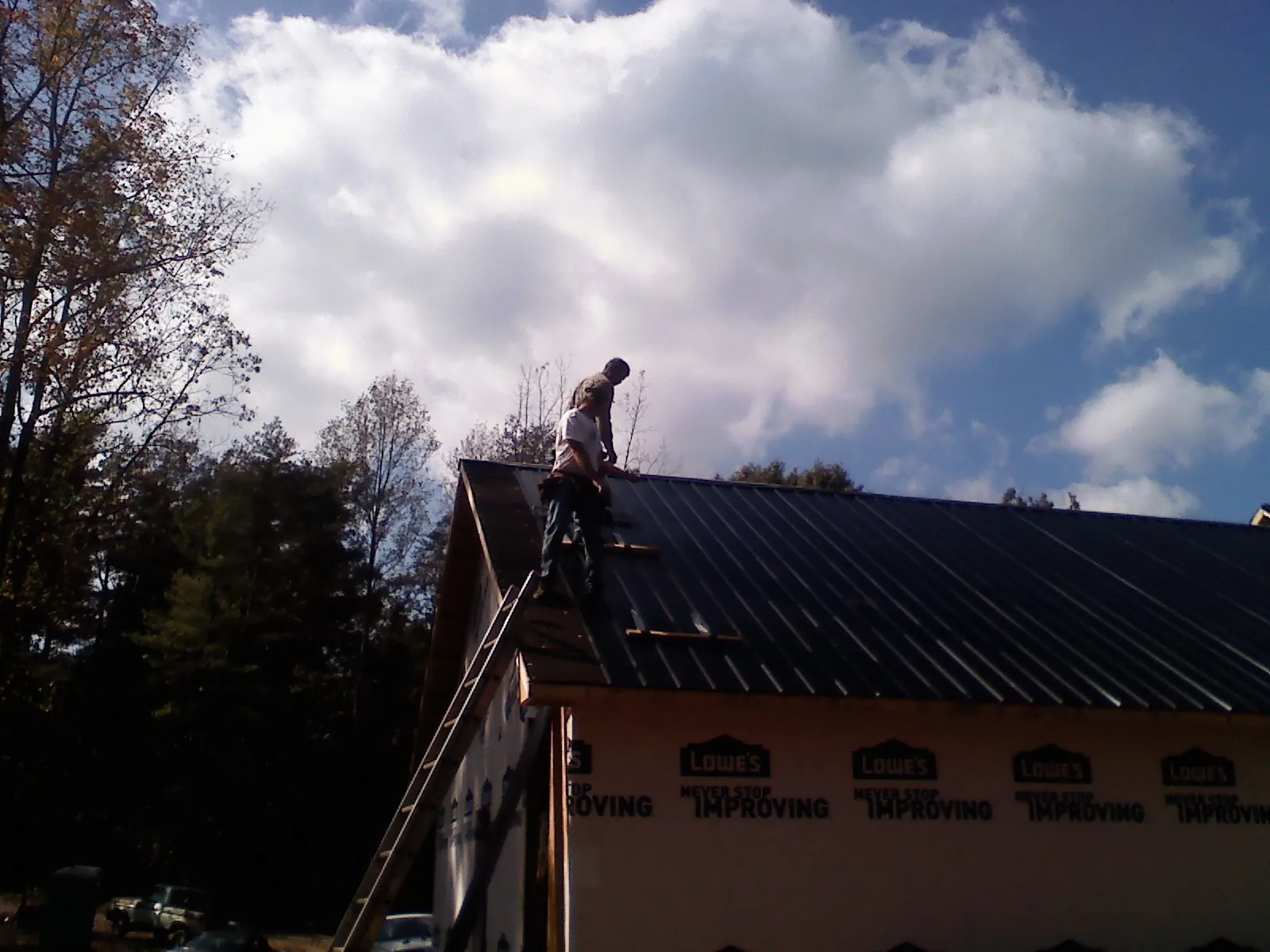 Roofer fastening dark metal panels high against a cloudy sky, from a Roof Inspection job in Cope